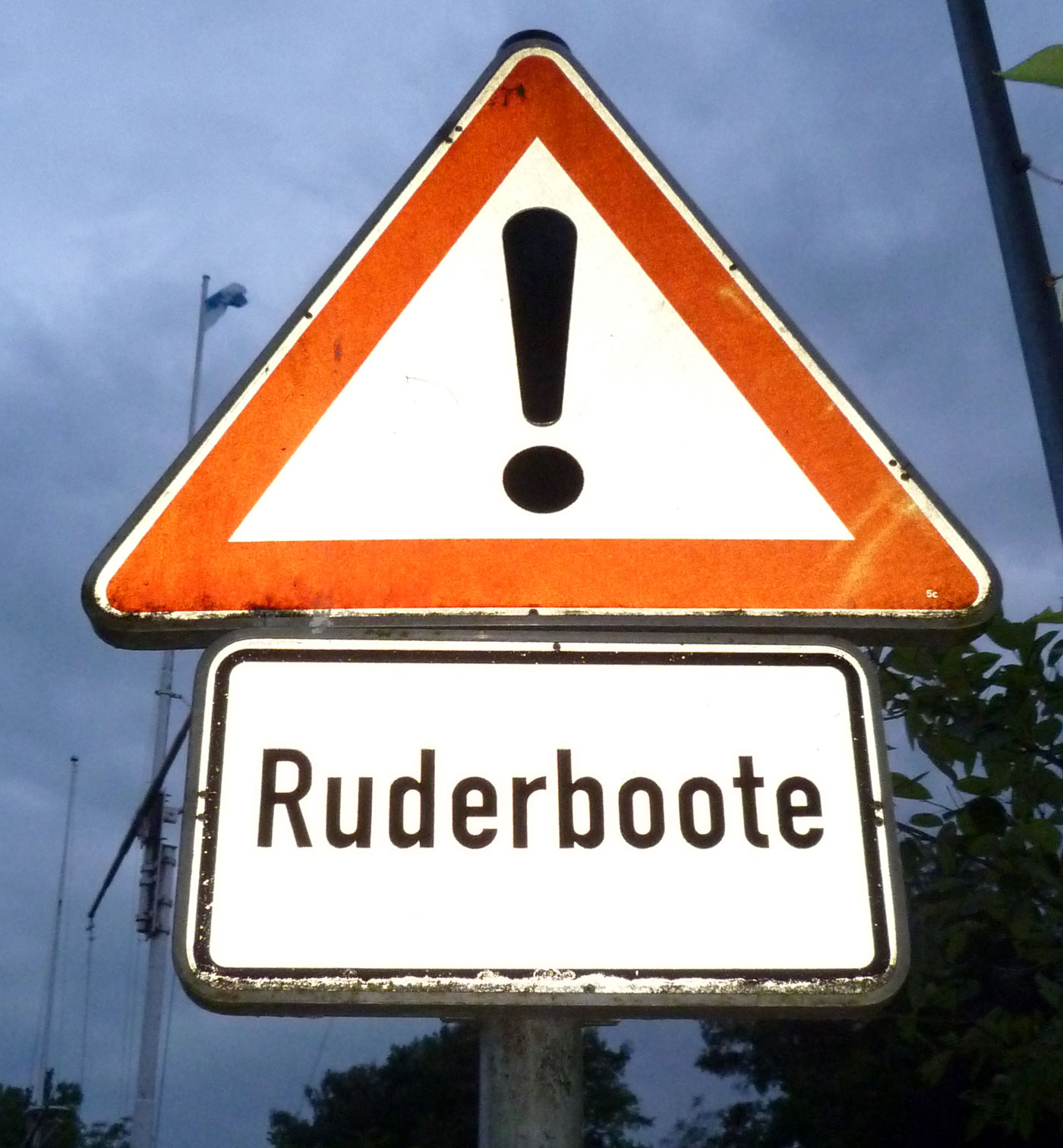 Verkehrsschild: Achtung! Ruderboote Ein Verkehrsschild (rot umrandetes Dreieck, das ein Ausrufezeichen umschließt) weist auf Ruderboote hin
