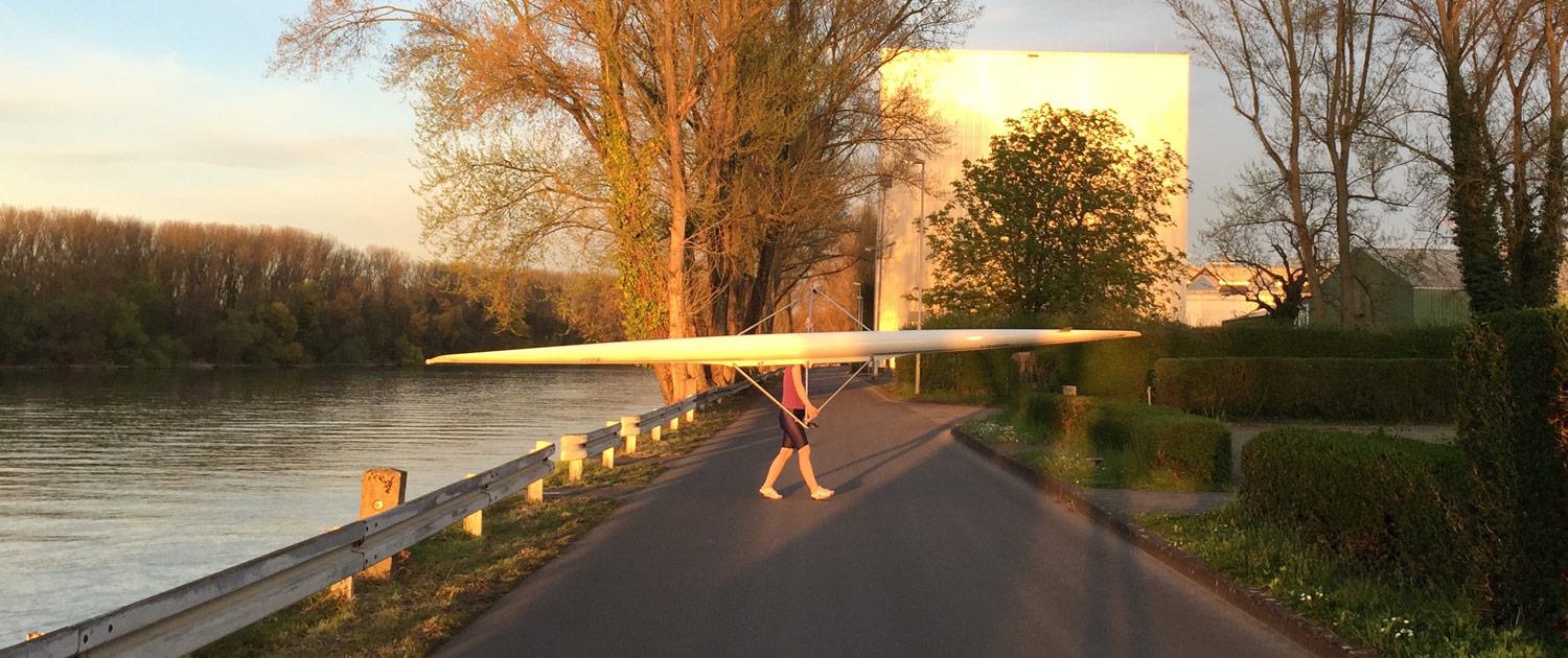 Ein Ruderer trägt sein Skif vom Steg hoch in die Bootshalle